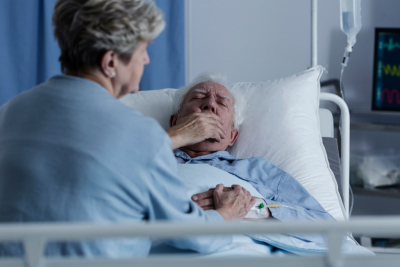 Elderly man with lung cancer lying in a hospital bed and coughing
